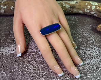 May include: A silver ring with a rectangular blue opal stone. The ring is on a model's finger.