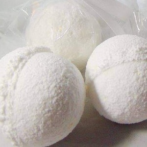 May include: Close-up of several white, round objects with a textured surface. Some are in clear plastic bags. The objects have a seam-like indentation, resembling a sports ball. The items are likely bath bombs or similar products.