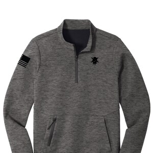 May include: A gray and black quarter-zip pullover sweatshirt with a zippered pocket on the left side. The sweatshirt has a black and white American flag on the left sleeve and a black logo on the chest that says "1.S.N."