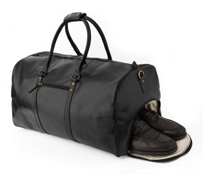 May include: Black leather duffel bag with a top handle and a zippered compartment. The bag has a separate shoe compartment with two black leather shoes inside.