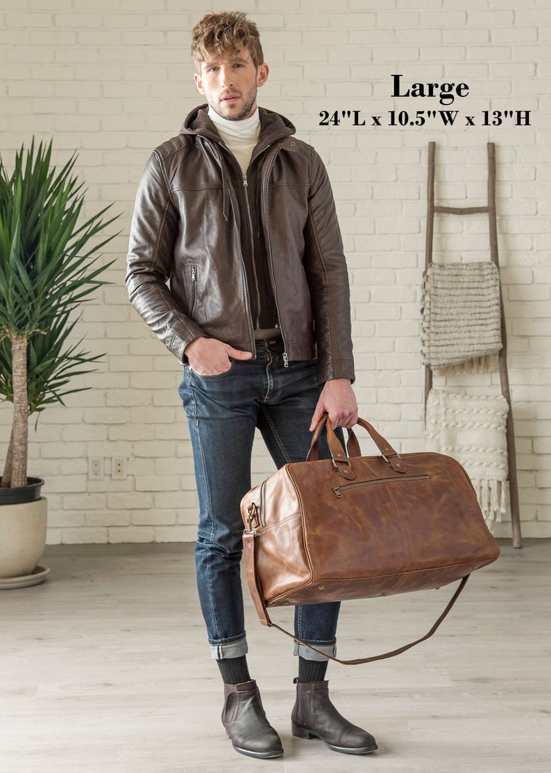 May include: A brown leather duffel bag with a shoulder strap, 24" long, 10.5" wide, and 13" high. The bag has a zipper closure and two top handles. The image also shows a brown leather jacket with a hood.