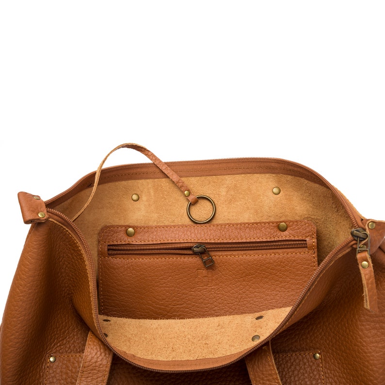 May include: A brown leather tote bag with a zipper closure and a small zippered pocket inside. The bag has a metal ring attached to the inside.