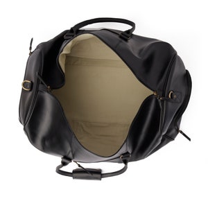 May include: A black leather duffel bag with a cream-colored lining. The bag is open and the zipper is visible. The bag has a top handle and a shoulder strap.