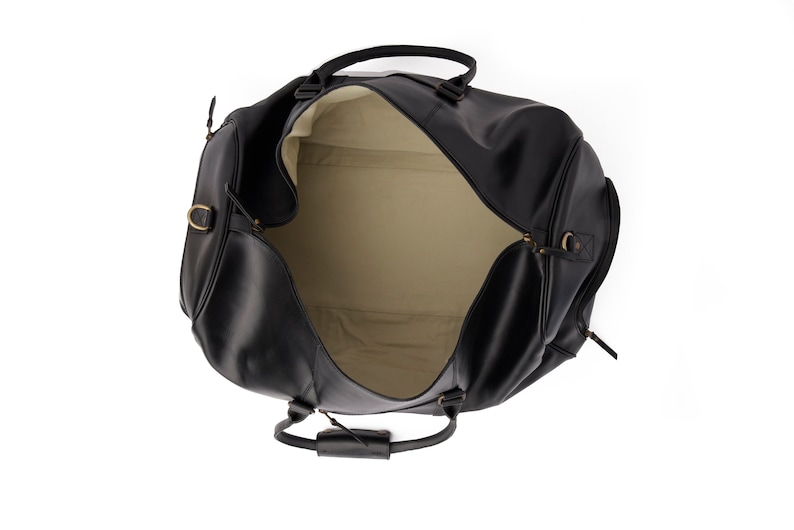 May include: A black leather duffel bag with a cream-colored lining. The bag is open and the zipper is visible. The bag has a top handle and a shoulder strap.