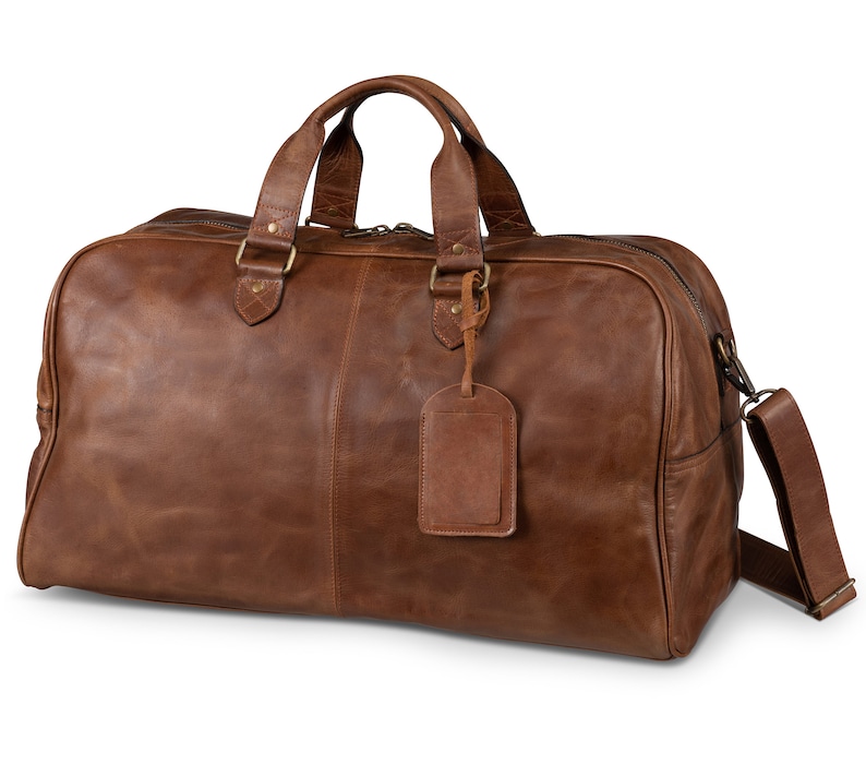 May include: A brown leather duffel bag with a top handle and a shoulder strap. The bag has a brass zipper and a brass tag.