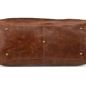 May include: A brown leather duffel bag with brass accents. The bag has a smooth, worn leather texture.