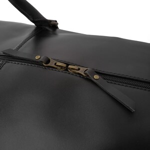 May include: Close-up of a black leather duffel bag with a zipper closure and brass hardware.