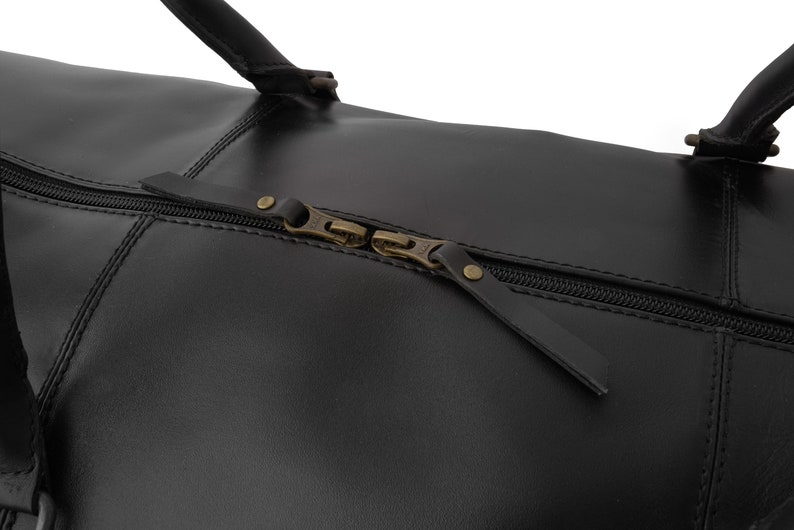May include: Close-up of a black leather duffel bag with a zipper closure and brass hardware.