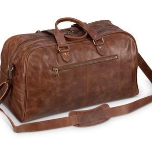 May include: A brown leather duffel bag with a top handle and a long shoulder strap. The bag has a zippered pocket on the front and a brass zipper pull.
