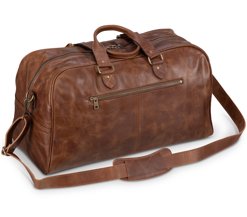 May include: A brown leather duffel bag with a top handle and a long shoulder strap. The bag has a zippered pocket on the front and a brass zipper pull.