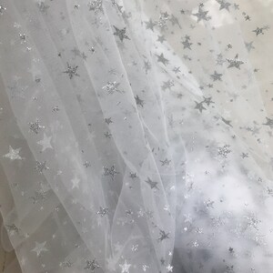 May include: White tulle fabric with silver glitter stars. The fabric is sheer and delicate, with a soft, flowing texture.