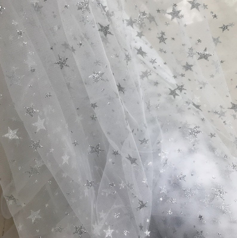 May include: White tulle fabric with silver glitter stars. The fabric is sheer and delicate, with a soft, flowing texture.