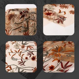 May include: Close-up of a beige sheer fabric with embroidered floral designs in shades of orange, brown, and green. The fabric has a delicate, airy texture.
