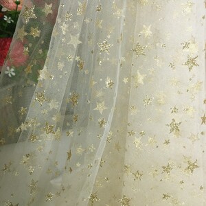 May include: White tulle fabric with a gold glitter star pattern.