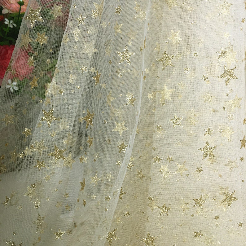 May include: White tulle fabric with a gold glitter star pattern.