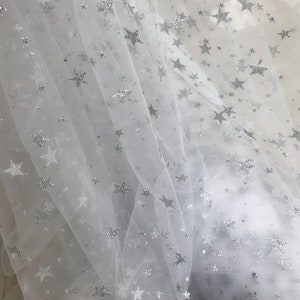 May include: White tulle fabric with silver glitter stars. The fabric is sheer and delicate, with a soft, flowing texture.
