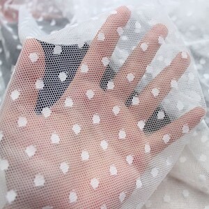 May include: White sheer fabric with small white polka dots. The fabric is delicate and has a soft texture.
