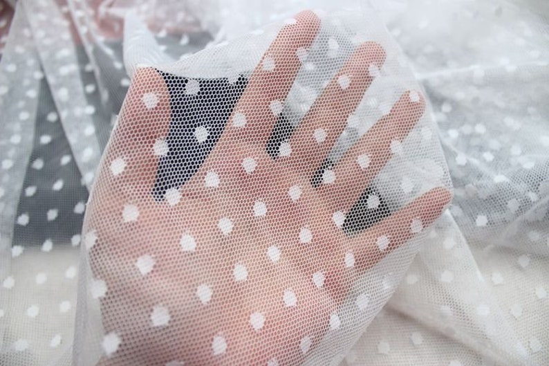 May include: White sheer fabric with small white polka dots. The fabric is delicate and has a soft texture.