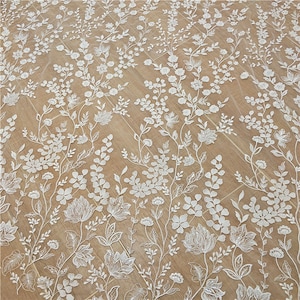 May include: White floral lace fabric with a delicate pattern of flowers and leaves. The lace is on a beige background.