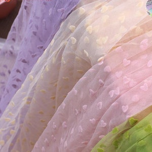 Puede incluir: Surtido de telas transparentes con un patrón de corazón en colores morado, crema, rosa y verde.