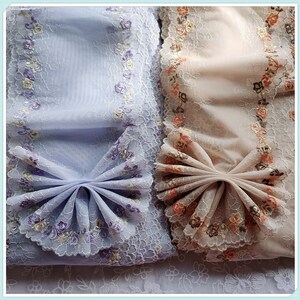 May include: Two pieces of sheer fabric with floral embroidery. The fabric on the left is light blue with purple flowers and the fabric on the right is peach with orange flowers.