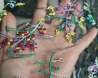 May include: Close-up of black sheer fabric with colorful floral embroidery. The embroidery features green stems with yellow, pink, and purple flower details. The fabric is held up, showcasing the intricate design and texture.