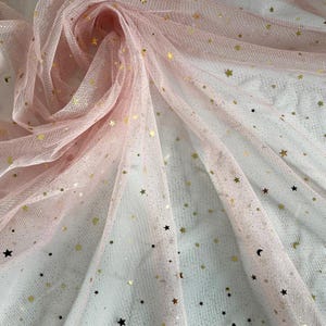 Puede incluir: Tela de tul rosa con estrellas doradas de purpurina y un sutil efecto degradado. La tela es transparente y delicada, perfecta para manualidades y proyectos de bricolaje.