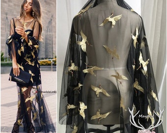 May include: Black sheer fabric with gold embroidered cranes. The fabric is draped over a dress form.