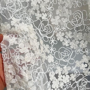 May include: White floral lace fabric with a delicate pattern of flowers and leaves. The lace is soft and sheer, and the design is intricate and elegant.