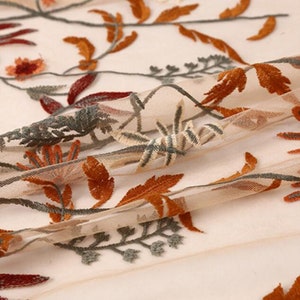 May include: Beige sheer fabric with embroidered floral designs in shades of orange, brown, and green.