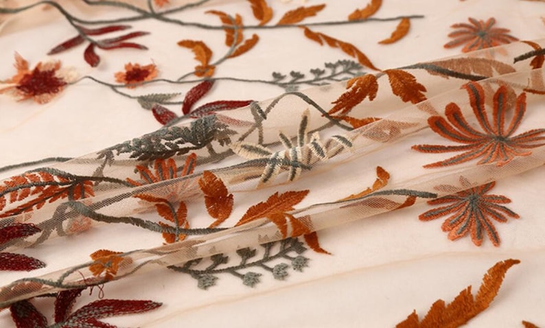 May include: Beige sheer fabric with embroidered floral designs in shades of orange, brown, and green.