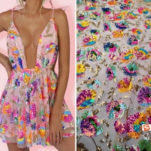 May include: A pink dress with a plunging neckline and a floral pattern made of colorful sequins. The dress is made of a sheer fabric and has a flowy skirt.