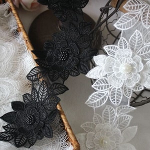 Könnte beinhalten: Zwei Stücke schwarzer und weißer Spitzenborte mit Blumendesigns. Die schwarze Spitzenborte hat in jeder Blume eine Perlenmitte. Die weiße Spitzenborte hat in jeder Blume eine perlmuttartige Perle in der Mitte.