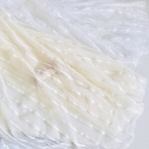 May include: White tulle fabric with a textured, dotted pattern. The fabric is soft and sheer, and it is perfect for crafting or decorating.