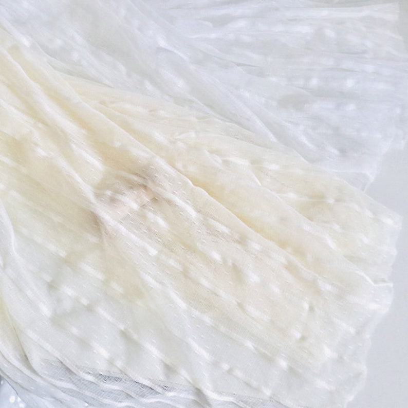 May include: White tulle fabric with a textured, dotted pattern. The fabric is soft and sheer, and it is perfect for crafting or decorating.