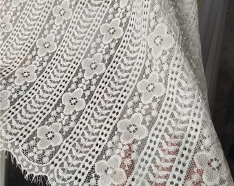 May include: White lace fabric with a delicate floral pattern. The lace has a scalloped edge and a slightly textured surface.