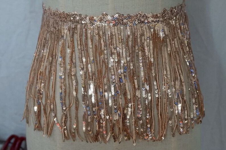 May include: Gold sequined fringe trim with a metallic sheen. The fringe is approximately 2 inches long.