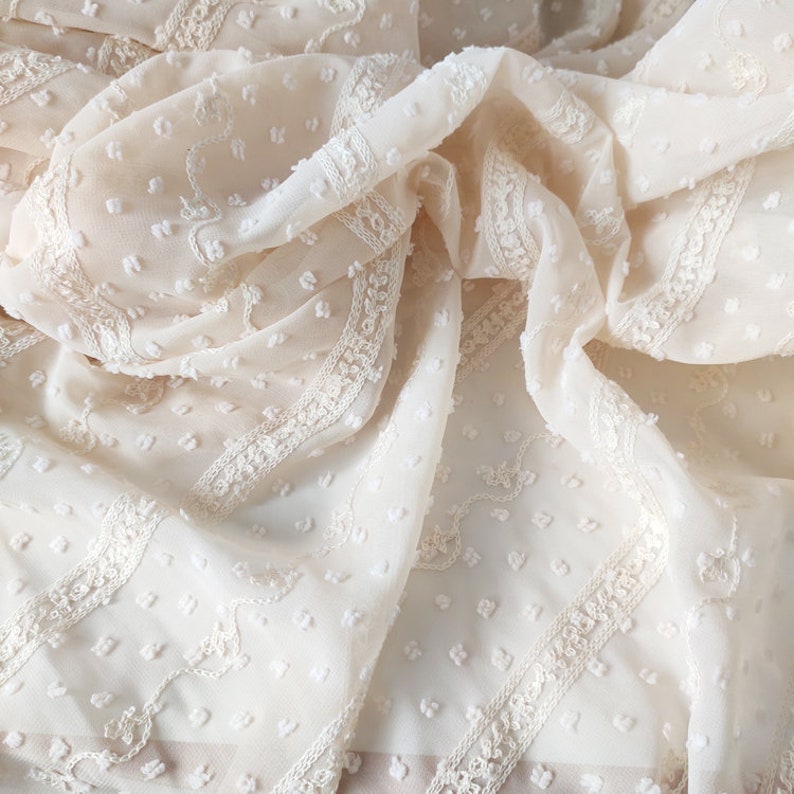 May include: White sheer fabric with a delicate embroidered pattern and small raised dots. The fabric has a soft, airy feel.