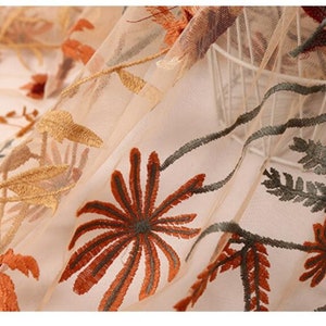 May include: Beige sheer fabric with embroidered floral designs in shades of brown, orange, and green.
