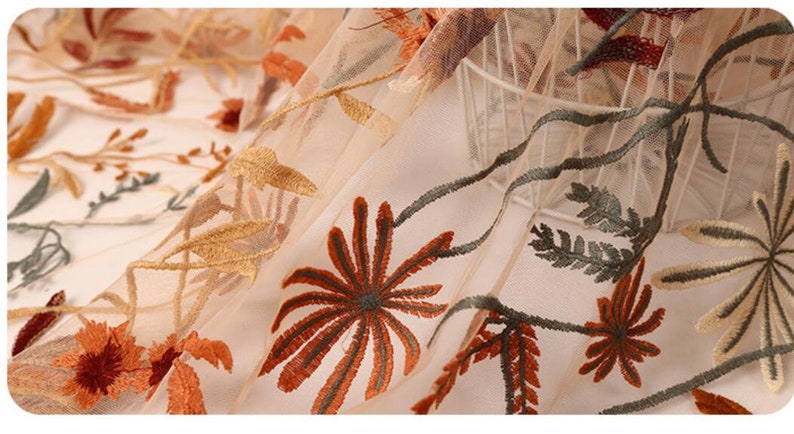 May include: Beige sheer fabric with embroidered floral designs in shades of brown, orange, and green.