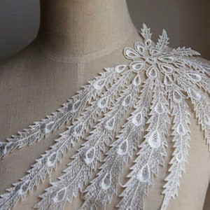 Peut inclure: Applique en dentelle blanche avec un motif de plume de paon. L'applique présente un groupe de plumes avec des détails en forme de larme.