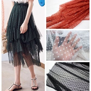 May include: A green tulle skirt with black polka dots and multiple layers. The skirt is shown on a model wearing sandals. The image also shows close-ups of different colors of tulle fabric with polka dots.