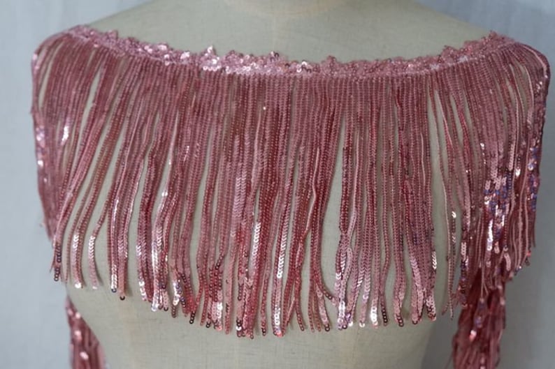 May include: Pink sequined fringe trim with a delicate, shimmering finish. This trim is perfect for adding a touch of glamour to any project.