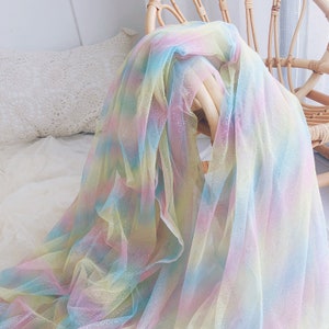 Könnte beinhalten: Ein Regenbogen-Ombre-Tüllstoff mit glitzernder Oberfläche. Der Stoff ist durchsichtig und hat eine weiche, zarte Textur.