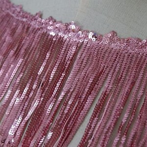 May include: Pink sequined fringe trim with a delicate, shimmering texture. This trim is perfect for adding a touch of glamour to any project.