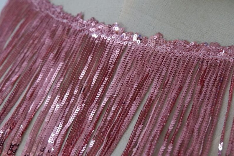 May include: Pink sequined fringe trim with a delicate, shimmering texture. This trim is perfect for adding a touch of glamour to any project.
