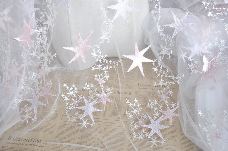 May include: White tulle fabric with pink and white embroidered stars. The fabric is sheer and delicate, perfect for crafting or adding a touch of whimsy to any project.