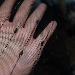 May include: Black sheer fabric with gold stripes and small dots. The fabric is delicate and has a soft, flowing texture.