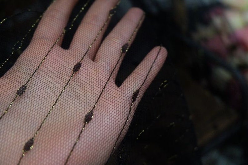 May include: Black sheer fabric with gold stripes and small dots. The fabric is delicate and has a soft, flowing texture.
