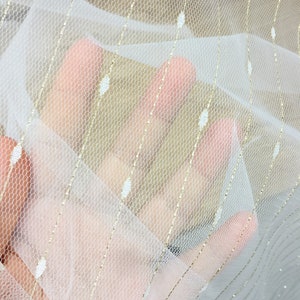May include: White sheer fabric with gold glitter stripes and small white dots.